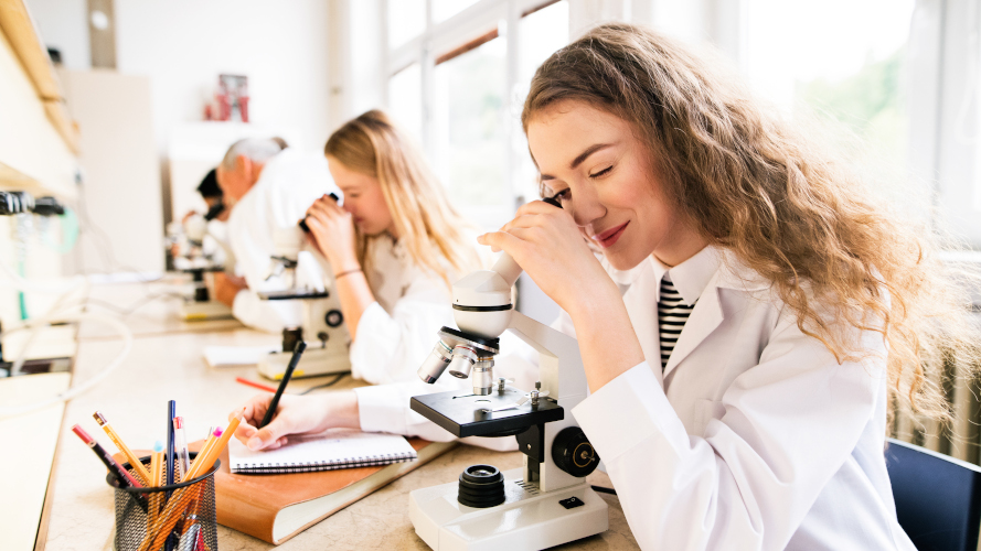 Ung kvinna i labbsal gör observationer med mikroskop.